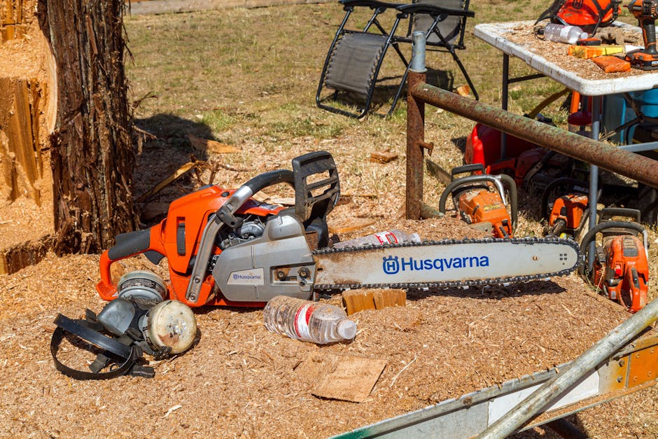 Husqvarna chainsaw and safety equipment surrounded by sawdust at a tree removal job site
